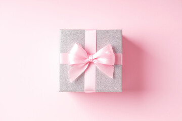 Silver glitter gift box with pink ribbon bow on pink background.