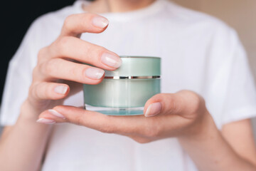 Female hands with natural pink manicure holding a transparent cream jar. Woman in white holds beauty product. Concept of body care and skin protection. Moisturizing lotion closeup. Facial skincare