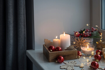 An artificial spruce branch, decorated with ivy leaves, apples and hawthorn berries. Lighted candles in wooden box, red glass balls, winter composition decorates interior on eve of Christmas