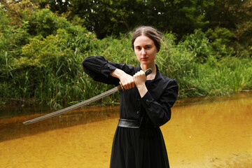 Woman in black dress holding a sword near the river