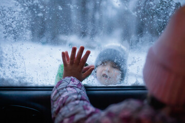Boy and girl touch each other with their palms through the frozen car window, winter road trip with the whole family, active weekend in any weather, winter car safety, help and support
