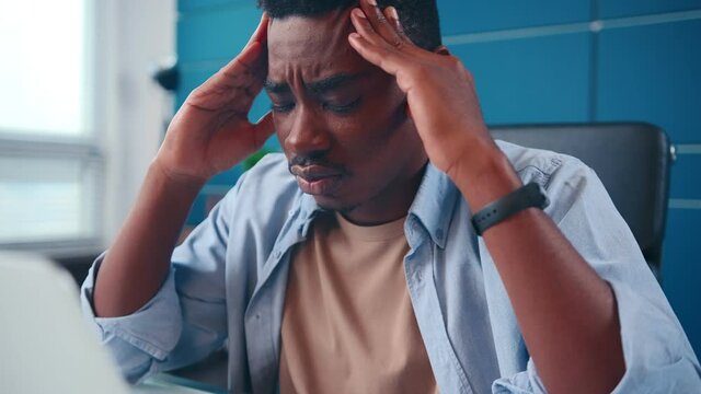 Disoriented African American businessman holding head with puzzled expression in front of laptop. Ethnic male stressed by business problems in office, freelancer suffers from overwork with deadlines.