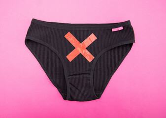 Black women's panties with a red cross on a pink background. Concept of female gynecological...
