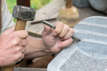 closeup of hands of a sculptor carving a stone slab with a chisel