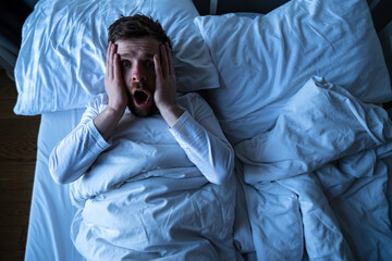 Man had a terrible nightmare, he woke up in horror, looking frightened with big eyes at the camera....