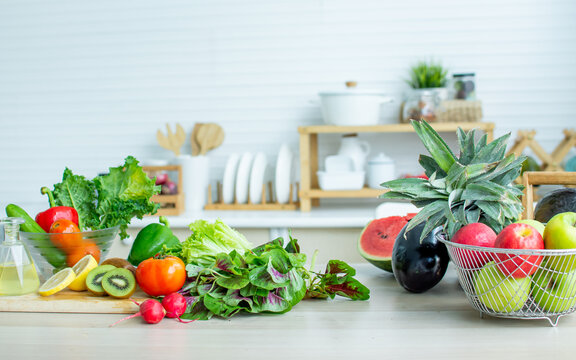 Background of green vegetables, fruits, lemon, kiwi, cherries and red tomatoes for good health decorated on wooden table in cozy white clean kitchen with copy space. Healthy food and interior Concept.