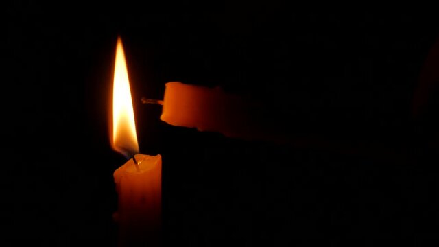 Burning candle in the darkness. Lighting candle with another one.