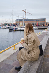 Girl drinks coffee on the background of yachts in the Marina. Hot drink in a paper cup. Disposable paper cup close up. Empty space for text, layout