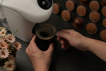 Closed up with a male hand holding a coffee cup under the coffee machine and decorated with coffee capsules.