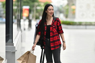 Photo of a fashionable woman carrying shopping paper bags in front of the shopping mall as a background.