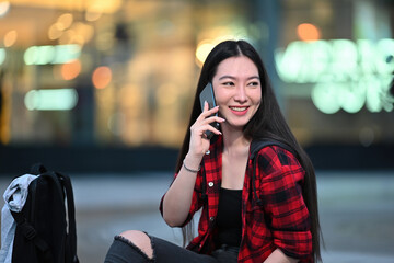 Fototapeta premium Photo of a beautiful woman talking on mobile phone while sitting in front of the shopping center.