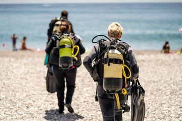 Three scuba divers with all equipment heading to the sea, Spain - obrazy, fototapety, plakaty