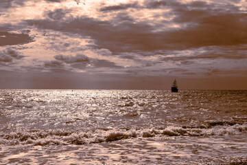 Seascape. A sailing ship sails across the sparkling sea against the background of a dark sky, golden toning. Sea trave