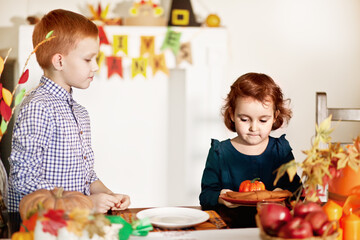 Kids served festive table and decorating living room for celebrating Thanksgiving day.