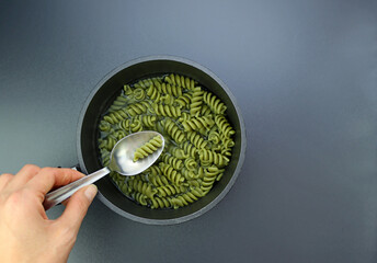 Green fusilli pasta in a spoon on a gray background. Fusilli in a ladle with water . Cooking pasta....