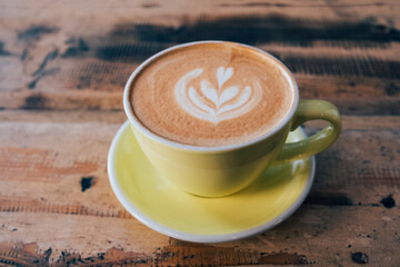 Cup of fresh delicious cappuccino coffee with beautiful latte art in the shape of leaf on shabby wooden background. Copy space. Morning hot drink.