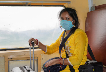 Young Indian woman in medical mask travelling in a train, sitting next to a window.