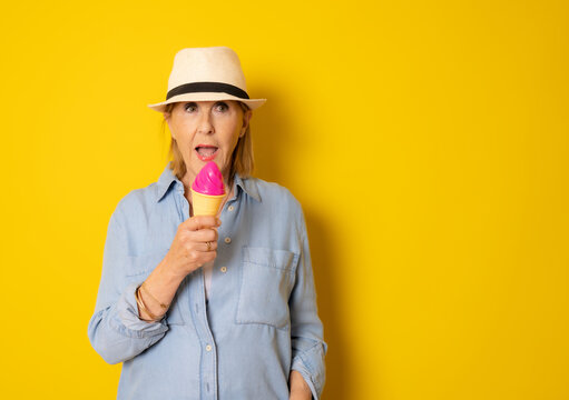 Senior woman in straw hat holding a cornet ice cream over isolated yellow background