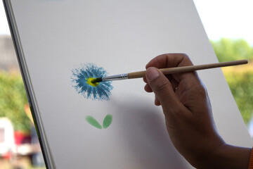 close-up of an Asian woman's hands hold a paintbrush to drawing flowers with watercolor outside the house. side view