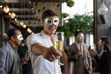 Young businessman smiling and wearing fantasy face mask and holding glasses of champagne for celebration in his company
