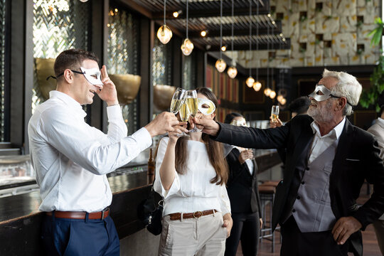 Group of diverse business people wear fantasy face mask and holding glasses of champagne for celebration in his company