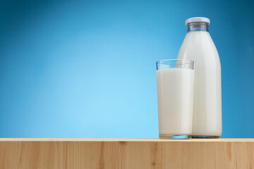 Bottle and glass of milk on wooden board and light blue background with copy space on the left.