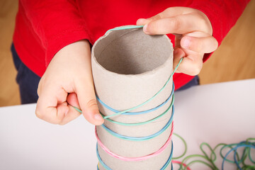 Little boy putting rubber bands or erasers on cardboard roll. Best creative game for early fine motor skills and logical thinking