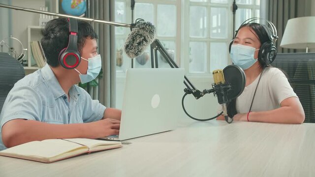 Wearing Protect Mask, Asian Boy Host Record Podcast Use Microphone Wear Headphone With Laptop Interview Guest Conversation For Content In His Home Studio. Content Creator Concept
