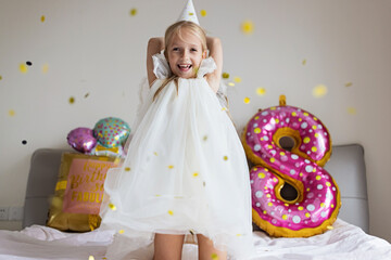 Indoor shot of pretty joyful cute adorable girl kid celebrating eight years old birthday with bright and colorful balloons with inscription words stay fabulous, wearing casual fashionable dress