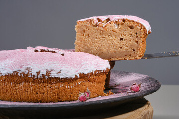 Sliced Bundt cake or Muffin cake with decorated icing pink sugar from roses on a wooden plate with small rosebuds. Shallow depth of field