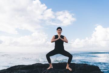Caucasian man in black sportswear smiling at camera during mediation time and hatha yoga practice, portrait of happy male enjoying leisure for namaste mindfulness pray at coastline seashore