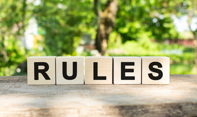 Five wooden blocks lie on a wooden table against the backdrop of a summer garden and create the word RULES.