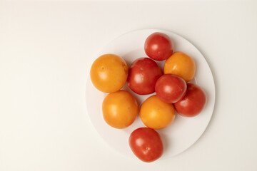 Healthy food composition of various fresh yellow and red tomato isolated on a white plate on grey background.