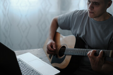 A man at home plays the guitar and looks into a laptop