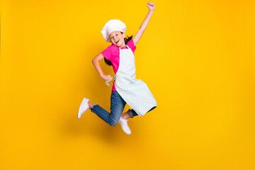 Photo of excited hero girl jump raise fist save your meal wear apron cap footwear isolated yellow...