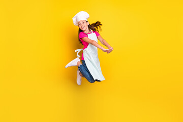 Photo of active adorable little girl jump hold arms wear apron cap shoes isolated yellow color background