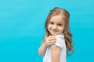 a little girl child with a patch on her arm after vaccination in a white T-shirt on a blue background in the studio, space for text, the concept of vaccination, health and medicine