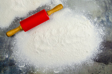 A pile of sifted flour and a rolling pin for rolling out the dough on a dark background of a concrete table top. Sprinkled flour on a cutting board. Space for text. Grainy surface, selective focus
