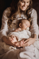 Beautiful young mother holds newborn baby girl in white lighter room at home. Tenderness cozy atmosphere