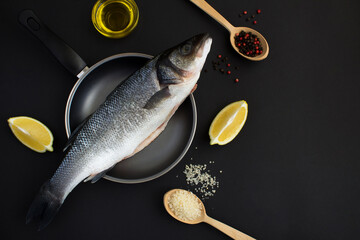 Top view of fish seabass on the frying pan on the black background. Close-up. Copy space.