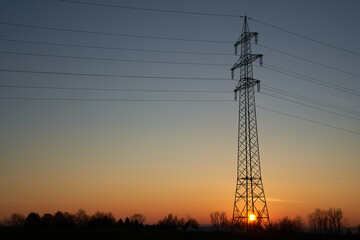 Single Electricity pylon (Strommasten) also overhead line pylon on the field. The sun sets on a clear evening sky. Side View. Copy Space.