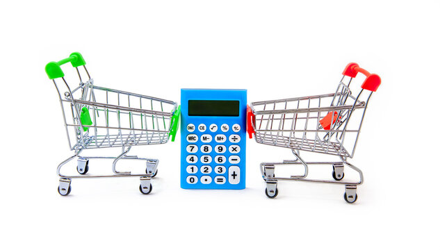 Electronic calculator and two grocery carts on white background. Concept of sales and purchases in stores. Discounts and savings. Iron miniature supermarket trolley hold electronic computing machine.