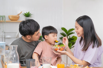 Happy refreshment family breakfast in morning, asian young parent father, mother and little cute boy, child having meal in kitchen eating together at home. Cheerful, enjoy cooking people.