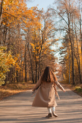 Young beautiful woman in beige coat walking on the road in autumn park
