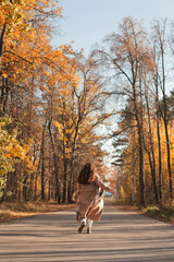 Young beautiful woman in beige coat running on the road in autumn park