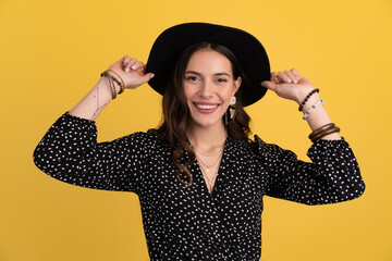 attractive woman posing isolated on yellow background wearing black hat and dress