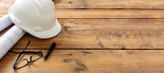 Construction safety concept. Building drawings and engineer white helmet on a wooden table, space