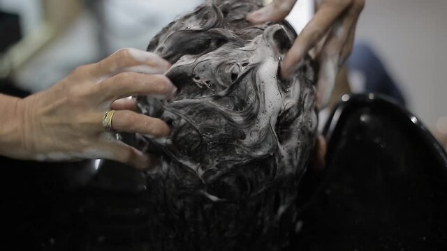 Joven tendida sobre lavabo de sal&oacute;n lav&aacute;ndose el pelo por un estilista profesional. La peluquer&iacute;a hace masajes en un sal&oacute;n de belleza.