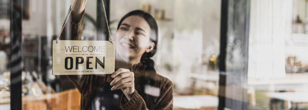 A Sign Hanging In Front Of The Shop Reads Open, The Female Employee Changed The Sign To Open The Shop After Preparing The Items. The Concept Of Opening A Shop.