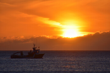 Obraz premium Sunset on the sea with a boat passing by on the beach of Doniños in Ferrol